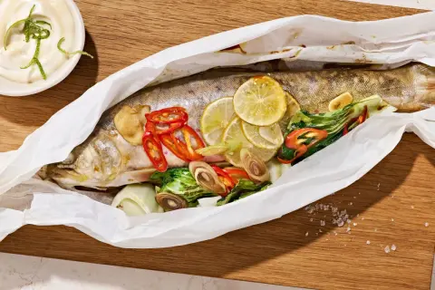 Ein ganzer Saibling, zubereitet in Papier mit Zitrone, Chili und Kräutern. Dazu eine Schale mit Dip. Perfekt zum Saibling essen.