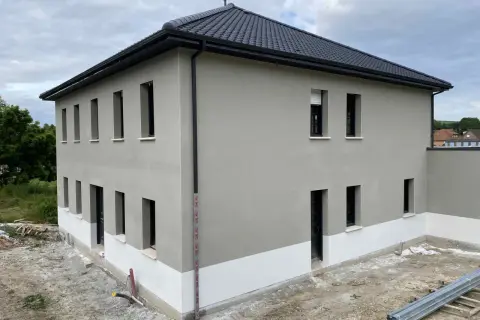 Maison neuve avec enduit de façade gris clair et soubassement blanc. Le chantier est en cours, montrant comment faire un enduit de façade.