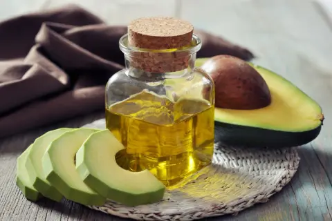 Flasche mit goldenem Persea gratissima oil neben frischen Avocadoscheiben und einer halben Avocado.