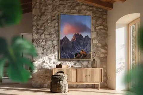 Quadro con montagne al tramonto, che cattura vibranti spazi colore. Zaino e mobile in legno completano l'arredo rustico.