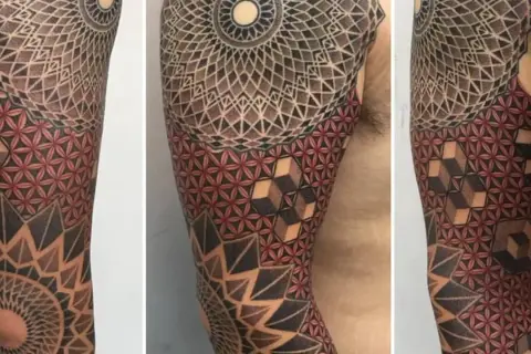 Brazo con tatuajes tradi geométricos, mandalas y flor de la vida en rojo y negro.
