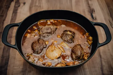 Herzhafte schmorgerichte im gusseisentopf, mit zarten Fleischrollen und Wurzelgemüse in einer dunklen Sauce.