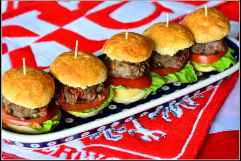 Pięć apetycznych mini burgery na zimno, ułożonych na talerzu, z pomidorami, sałatą i mięsem. Idealne na letnie przyjęcie.