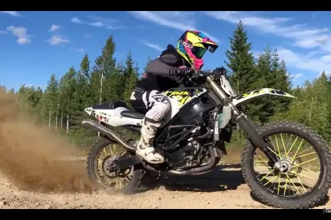 Motocyklista w kolorowym kasku pędzi na crossie, wzbijając tumany kurzu.