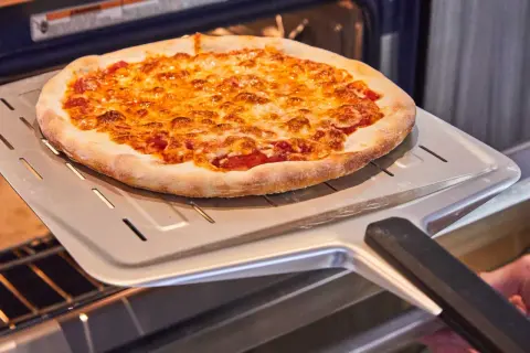Une délicieuse pizza maison dorée et gratinée sort du four sur une pelle à pizza.