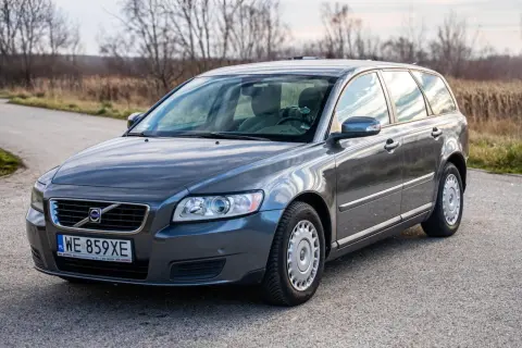 Szary Volvo V50 2.0D na drodze, z drzewami w tle.