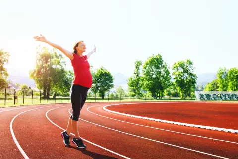 Donna incinta con le braccia aperte su una pista da corsa, dimostra che si può correre in gravidanza.