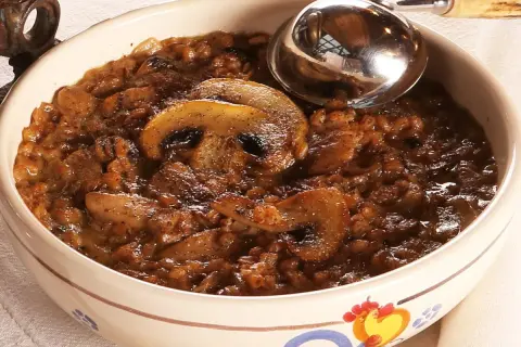 Una ciotola decorata con una ricca zuppa di farro e funghi, pronta per essere servita con un mestolo.