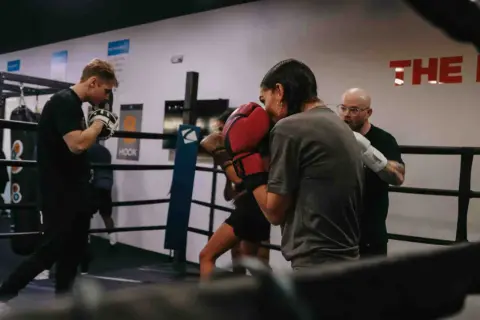 Intense soviet boxing training session in a ring. A coach observes as two boxers spar, their gloves a blur of motion.
