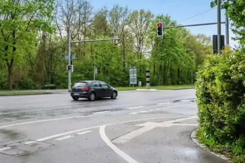 Ein dunkler Golf fährt über eine nasse Straße, die Ampel zeigt rot. Hoffentlich hat er nicht bei rot geblitzt.