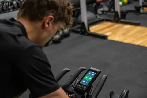 Mężczyzna na rowerze stacjonarnym sprawdza dane treningowe. Czy to już czas na test FTP?