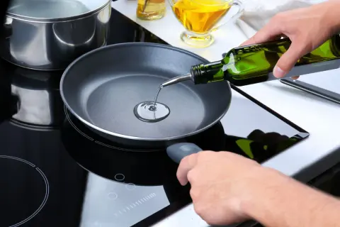 Mani versano olio extravergine in una padella su un piano cottura a induzione. Si può friggere con olio extravergine per un gusto autentico.
