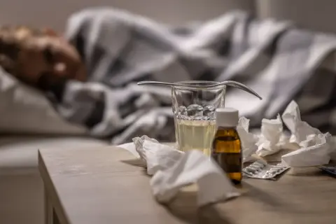 Sjuk person i sängen med medicin, glas vatten och näsdukar på bordet. Viktigt för att minska sjukfrånvaro.