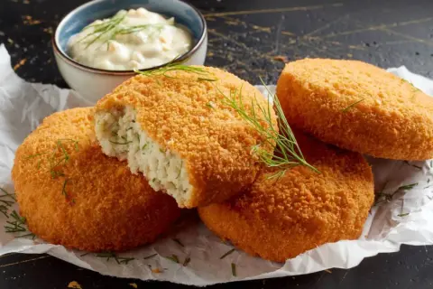 Crujientes croquetas de merluza doradas, una partida revela su interior tierno. Servidas con una cremosa salsa y eneldo fresco.