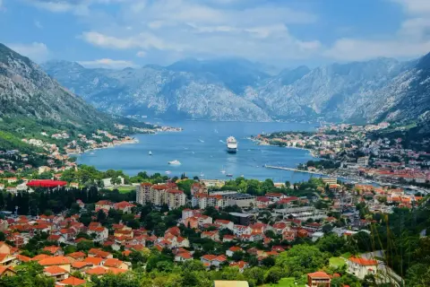 Vacker vy över Kotorbukten i Montenegro. Ett kryssningsfartyg ligger för ankar i det blå vattnet, omgivet av berg och en stad med röda tak. Montenegro mat kan avnjutas med en sådan här utsikt.