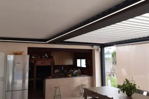 Un moderno patio de luces con normativa de iluminación LED integrada, que ilumina una cocina exterior y zona de comedor.