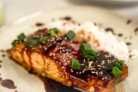 En saftig asiatisk lax med glansig teriyakisås, toppad med sesamfrön och salladslök, serveras med ris.