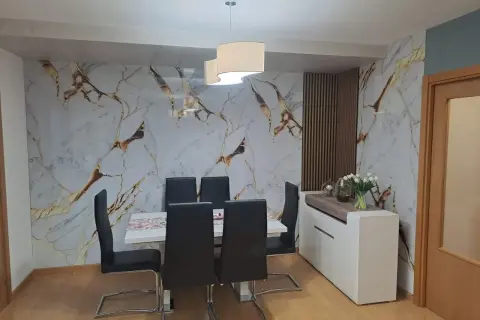 Comedor moderno con pared de mármol y oro, sillas negras y aparador blanco. El cloruro de polivinilo (PVC) es un material versátil.