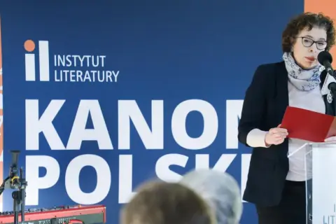 Kobieta przemawia na tle napisu "Instytut Literatury" i "Kanony Polskie", prezentując dzieła najwybitniejszych polskich pisarzy.