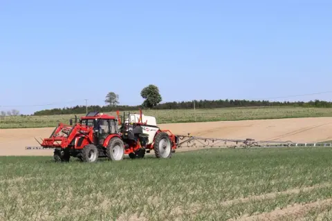 Czerwony traktor z opryskiwaczem na polu. Prawidłowa kolejność mieszania środków ochrony roślin zapewnia skuteczne działanie.