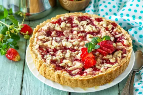 Pyszna tarta z truskawkami i kruszonką, ozdobiona świeżymi owocami i miętą, kusi apetycznym wyglądem.