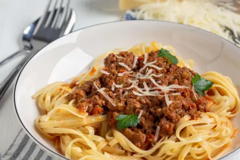 Teller mit Spaghetti Bolognese, garniert mit Parmesan und Petersilie. Ja, man kann gekochte Spaghetti Bolognese einfrieren.