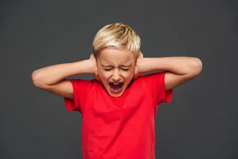 Bambino con capelli biondi, occhi chiusi e bocca spalancata, copre le orecchie con le mani. Rappresenta una crisi di rabbia nei bambini di 10 anni.