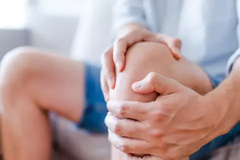 Dłoń obejmująca bolące kolano.