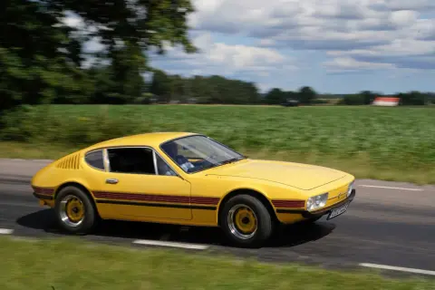 Gul vw sp2 susar fram längs en landsväg, med gröna fält och moln som suddas ut i bakgrunden.