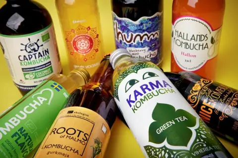 Flera flaskor kombucha, en dryck som många anser vara nyttig, ligger utspridda. Olika märken som Captain Kombucha, Karma Kombucha och Hallands Kombucha syns tydligt.