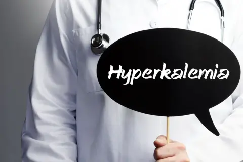 Lekarz w białym fartuchu ze stetoskopem trzyma czarną chmurkę z napisem "Hyperkalemia". Oznacza to podwyższony potas we krwi.