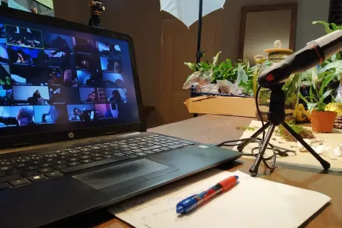 Laptop z ekranem pełnym twarzy uczestników online, mikrofon i notatki. Wirtualne spotkanie, które integruje zespół.