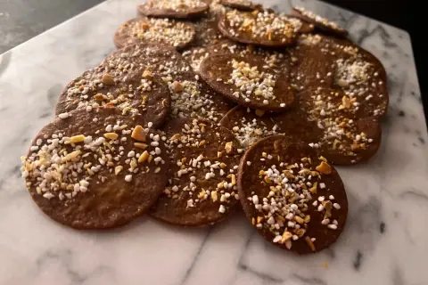 En hög med runda, mörka kakor med mandelmjöl och choklad, toppade med hackade nötter och pärlsocker. Perfekta till fikat!