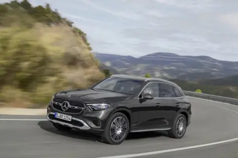 Czarny Mercedes GLC 200 4MATIC pokonuje zakręt na górskiej drodze, otoczony zielonymi wzgórzami i skalistymi zboczami.
