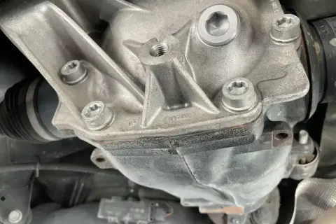 Metalowy dyferencjał z widocznymi śrubami i osłoną przegubu napędowego.