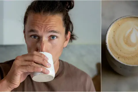 Man med blå ögon dricker en vacker latte hemma. Kaffet har ett hjärtformat mönster i skummet.