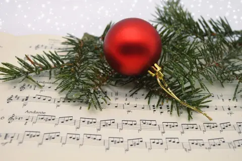 Boule rouge sur partition de "Minuit Chrétien", entourée de branches de sapin givrées. La musique de Noël prend vie.