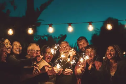 Familie feiert mit Wunderkerzen unter Lichterketten. Ein Lächeln, das die Bedeutung eines 75. Hochzeitstages widerspiegelt.