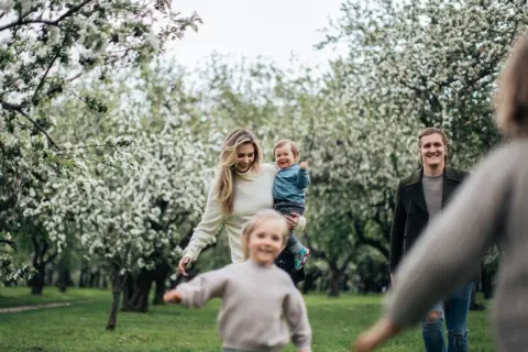 Radosna majówka z dziećmi w kwitnącym sadzie. Rodzina cieszy się wiosennym dniem wśród drzew.