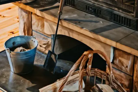 Metalowy kubeł z popiołem i kosz na drewno przy kamiennym kominku. Latem śmierdzi z kominka jak się nie pali, ale przygotowania do jesieni trwają.