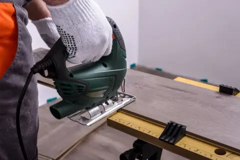 Mit einem Stichsäge wird Laminat schneiden. Ein Handwerker mit Handschuhen arbeitet präzise.
