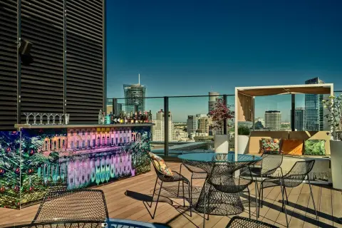 Elegancki ether rooftop bar z widokiem na miasto. Kolorowy bar, stoliki i wygodne fotele zapraszają do relaksu.