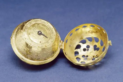 Esfera dorada ornamentada de un primer reloj mecánico, abierta para mostrar su intrincado interior.