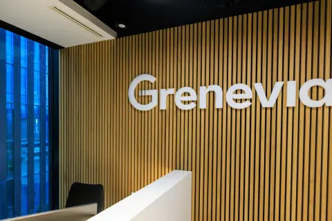 Nowoczesne biuro z logo Grenevia na drewnianej ścianie. Za oknem błękitny, deszczowy krajobraz miejski.