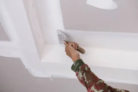 Mano aplicando masilla para techo escayola con espátula, alisando juntas y esquinas para un acabado perfecto.