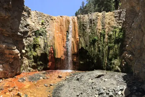 Cascada rojiza y verde en un cañón rocoso, ideal para senderismo en Palma de Mallorca.