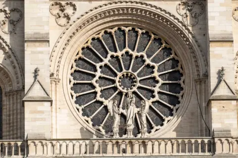 Ein Rosettenfenster im Stil der Gotik-Kunst, umrahmt von Steinfiguren und filigranen Verzierungen an einer Kathedrale.