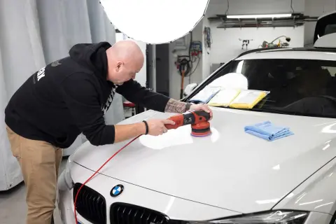Man polerar en vit bil med maskin för att få en perfekt finish.