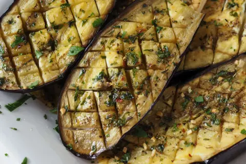 Gegrillte Auberginenhälften, mit Kräutern und Knoblauch gewürzt, bereit zum Servieren. Ein köstliches Gericht, das die Aromen des Ofens einfängt.