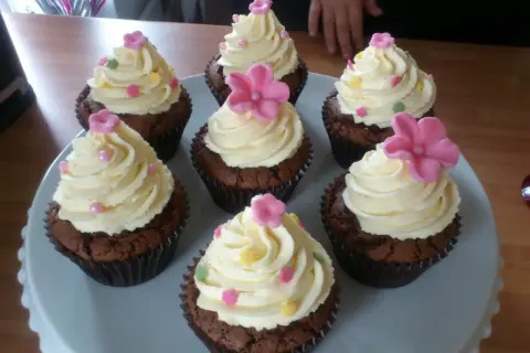 Sju chokladmuffins med fluffig vit choklad frosting, dekorerade med rosa blommor och strössel. Perfekt för ett kalas!